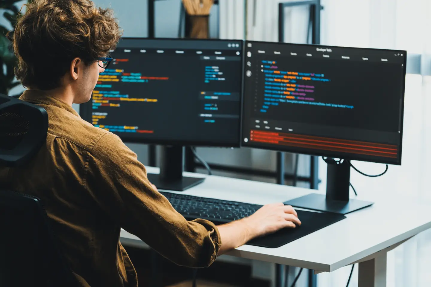 Programista pracujący nad kodem strony internetowej na dwóch monitorach. Wykorzystanie sztucznej inteligencji i asystentów AI w web developmencie.