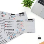 Rozłożone okładki na dowody rejestracyjne z trzykolorowym nadrukiem usług Moto Centrum leżące na białym blacie obok szarego laptopa.