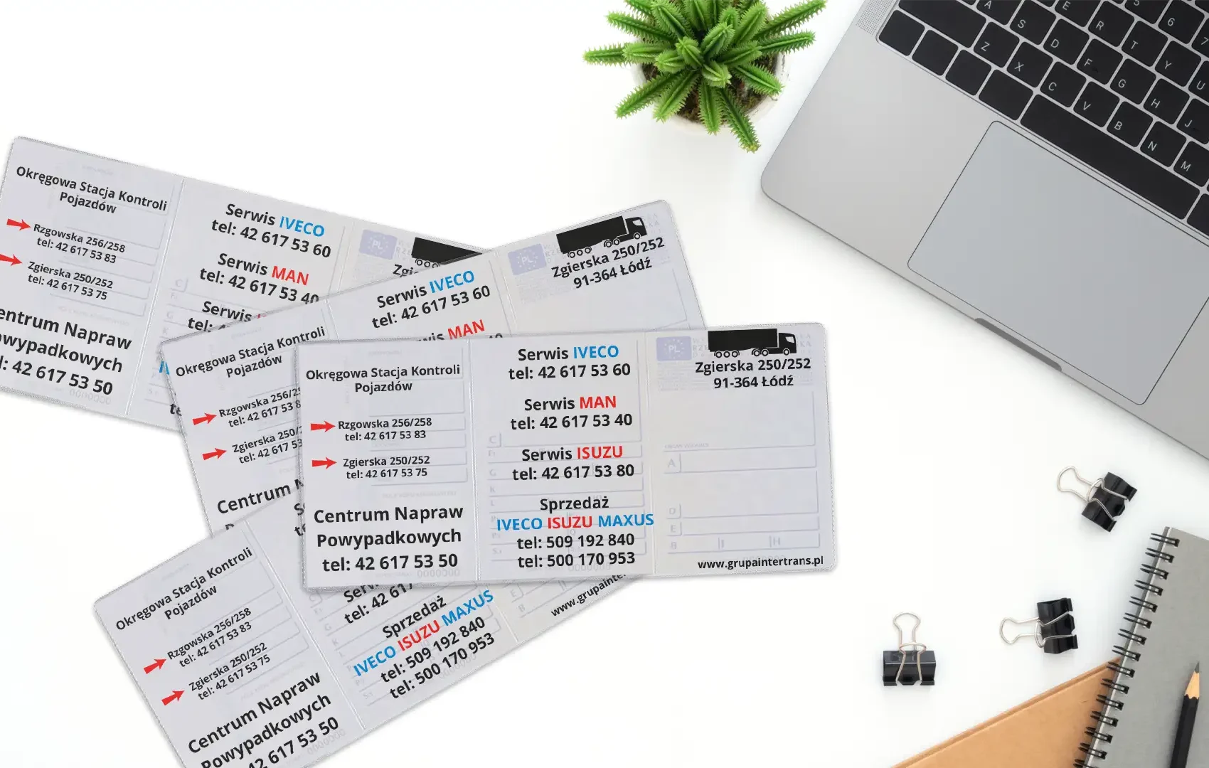 Rozłożone okładki na dowody rejestracyjne z trzykolorowym nadrukiem usług Moto Centrum leżące na białym blacie obok szarego laptopa.