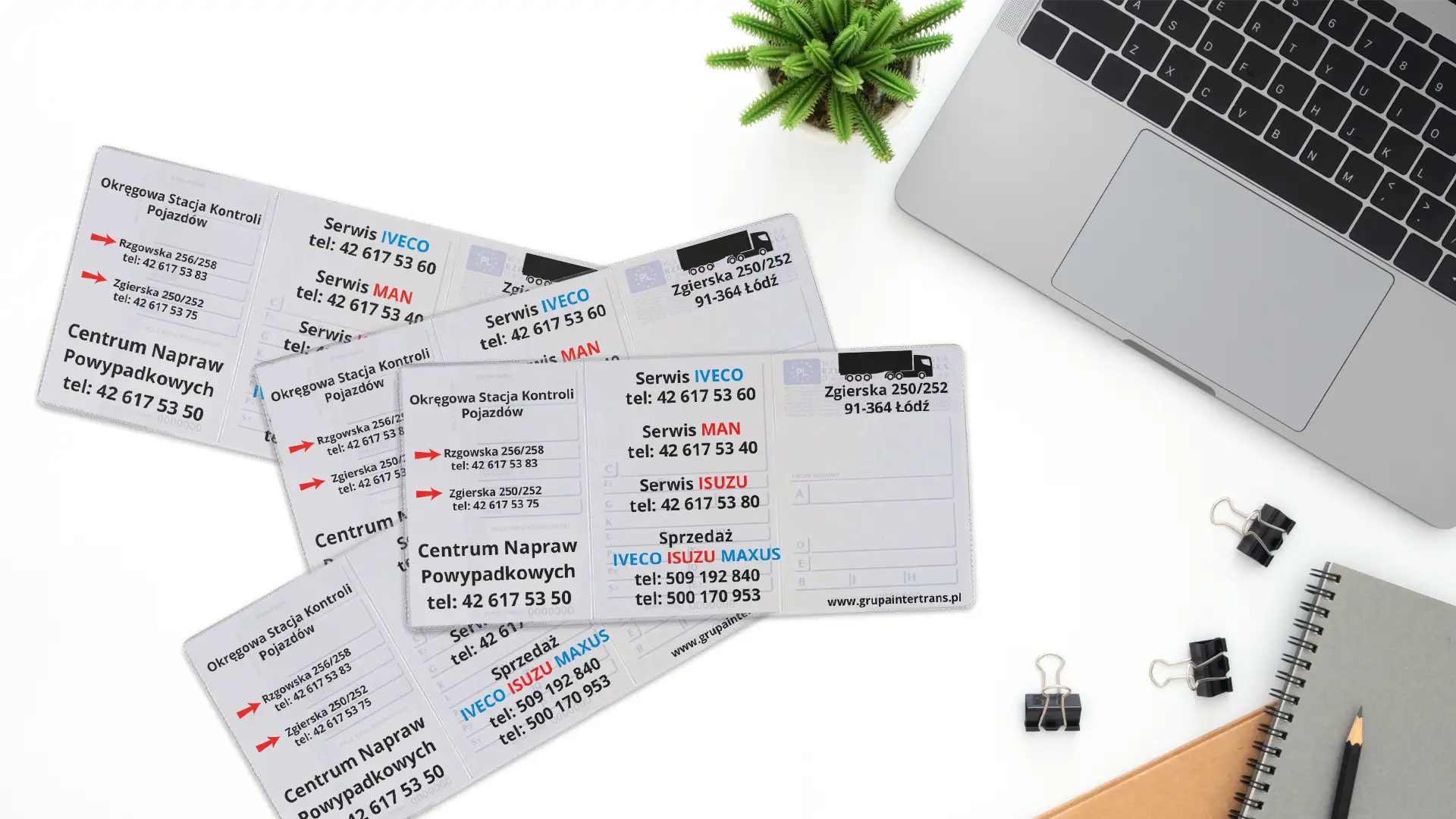 Rozłożone okładki na dowody rejestracyjne z trzykolorowym nadrukiem usług Moto Centrum leżące na białym blacie obok szarego laptopa.