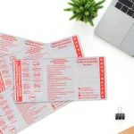 Cztery rozłożone okładki na dowody rejestracyjne z czerwonym nadrukiem stacji OSKP Borowa, leżące na białym biurku obok laptopa i roślinki.