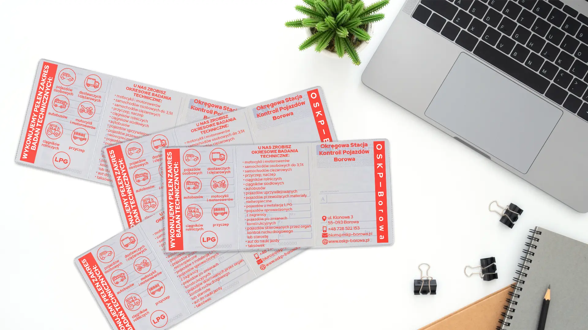 Cztery rozłożone okładki na dowody rejestracyjne z czerwonym nadrukiem stacji OSKP Borowa, leżące na białym biurku obok laptopa i roślinki.