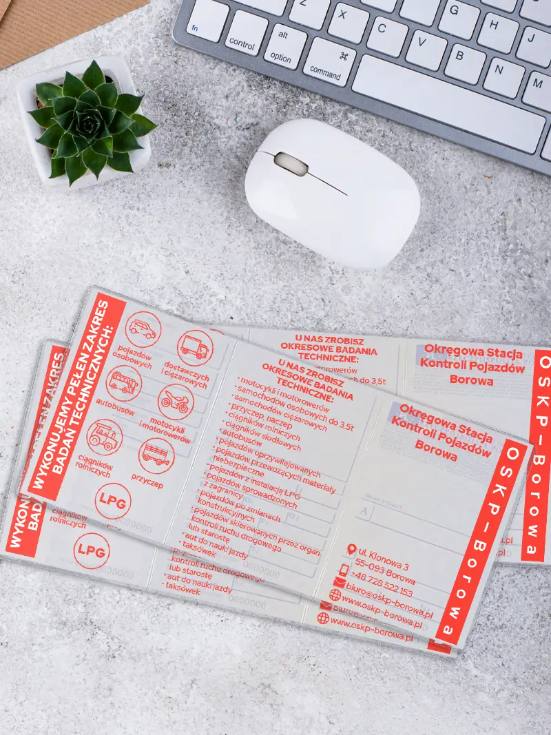 Zbliżenie na wnętrze okładki na dowód rejestracyjny z nadrukiem OSKP Borowa prezentującym ikony pojazdów, leżącej na jasnym blacie obok białej myszki.